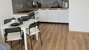 A modern kitchen with white cabinets, a microwave, a sink, and a dining area with a table and chairs. - Malta View Prestige (Poznań)