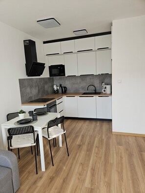 A modern kitchen with white cabinets, a microwave, a sink, and a dining area with a table and chairs. - Malta View Prestige (Poznań)