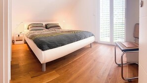 Et soveværelse med seng, sengebord, lampe, stol og udsigt ud af vinduet.