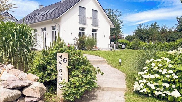 En hvid bygning med en stenhængt sti, der fører til indgangen, omgivet af grøn vegetation og et skilt med teksten 'SPICHESTRASSE 6'.