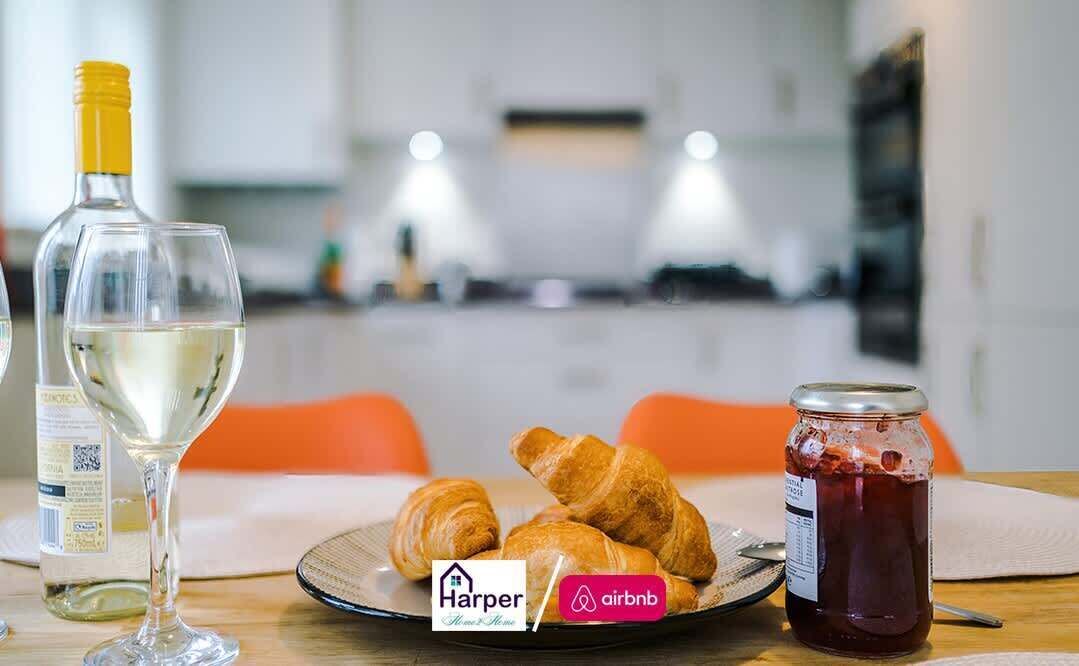 Et spisebord med en vinflaske, et glas, croissanter og et syltetøjsglas.
