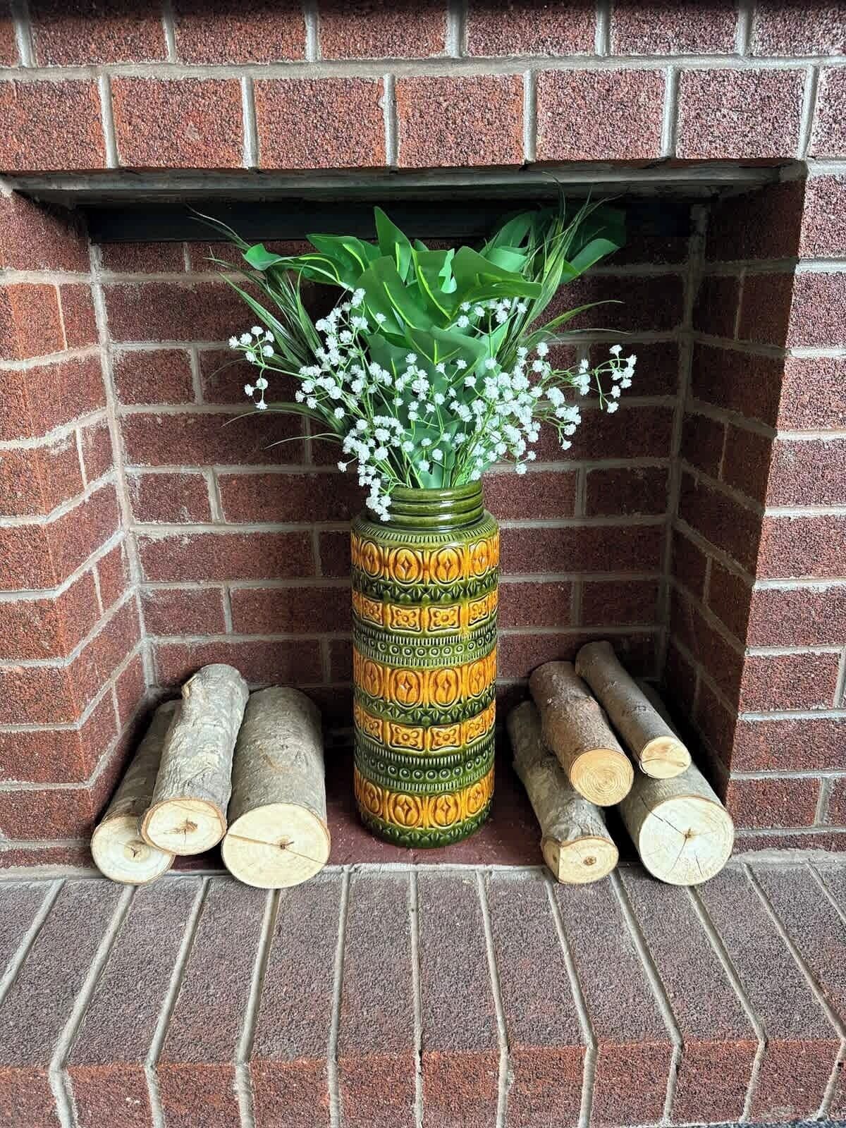 A brick fireplace with a decorative vase of flowers and logs.