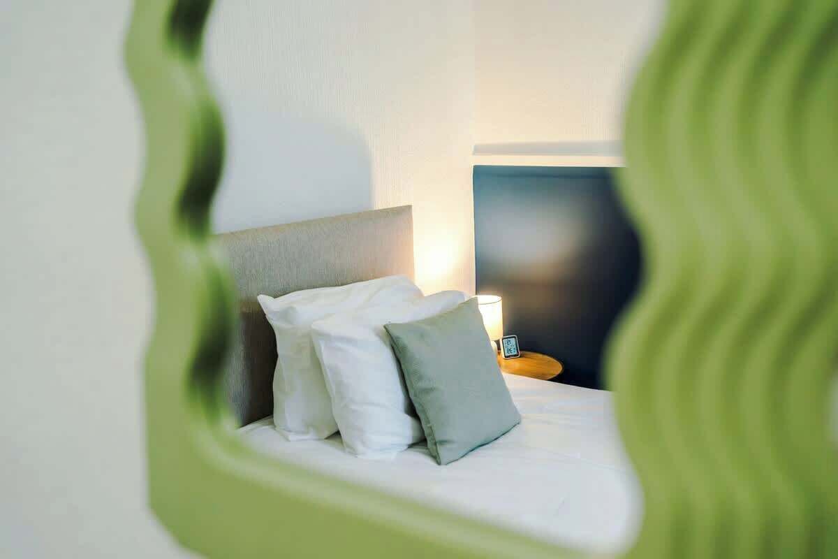 Un lit bien fait, avec des oreillers, une table de chevet avec une lampe et un téléviseur fixé au mur.