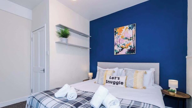 Ein Hotelzimmer mit Bett, Nachttisch, einer an der Wand befestigten Ablage mit Pflanze und einem Gemälde.
