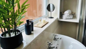 Ein Badezimmer mit einer Badewanne, einem Blumentopf, einem schwarzen Behälter und einem Spiegelbrett.