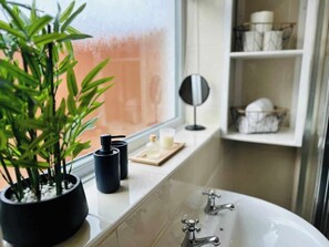 Ein Badezimmer mit einer Badewanne, einem Blumentopf, einem schwarzen Behälter und einem Spiegelbrett.