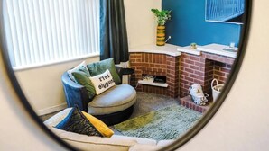 Ein gemütliches Zimmer mit einem runden Spiegel, einem Kamin aus Ziegelsteinen, einer bequemen Sitzecke und einer kleinen Pflanze auf einem Regal.