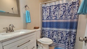 Ein Badezimmer mit Waschbecken, Toilette, blauer Duschvorhang und blauer Badmatte.