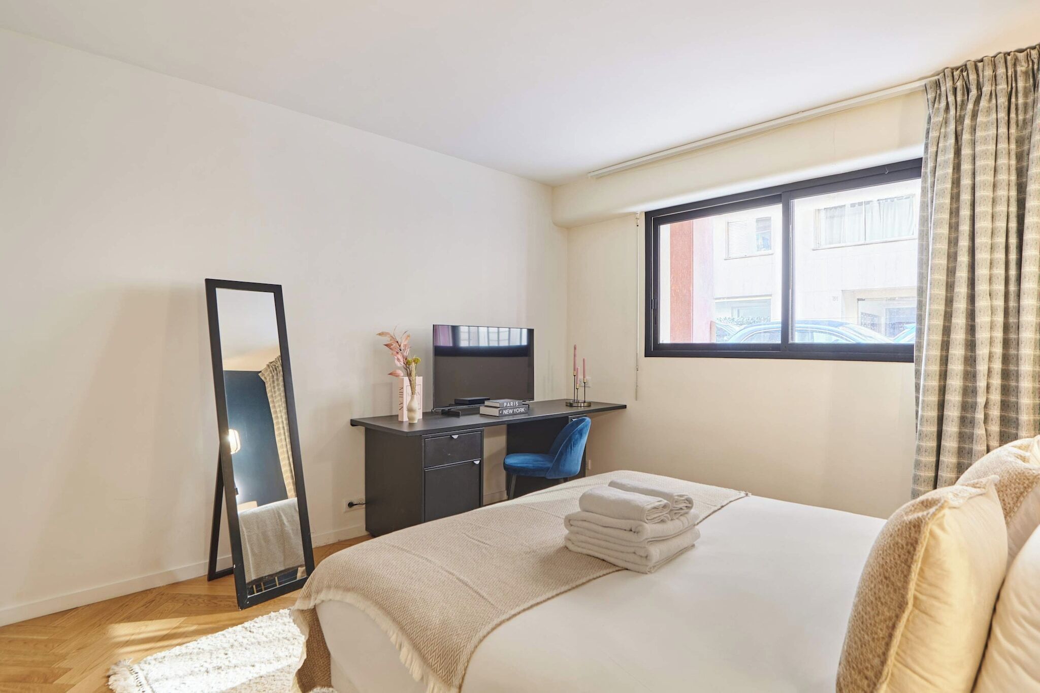 Un dormitorio con cama, escritorio, silla, espejo y ventana con cortinas.
