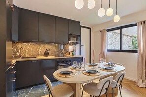 Une cuisine moderne avec des meubles de couleur sombre, un pare-feu en marbre et un coin repas aménagé pour quatre personnes, avec une table ronde et des chaises.
