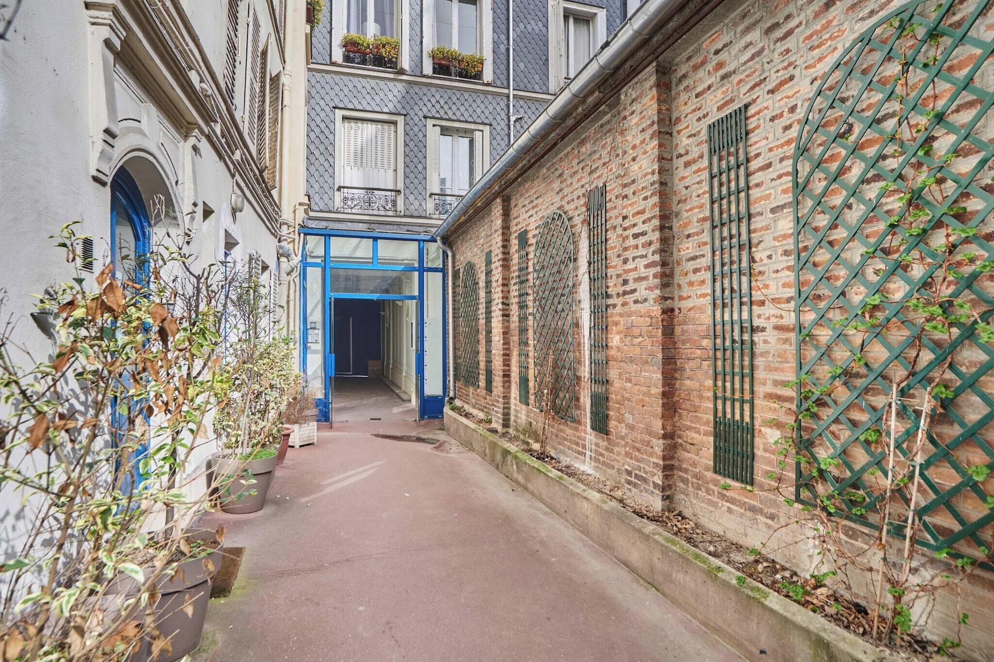 A narrow alleyway with a blue door, brick buildings, and potted plants.