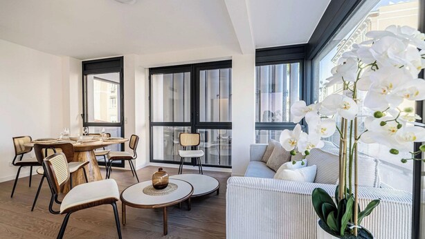 Een moderne woonkamer met een eethoek, grote ramen en een potorkidee.