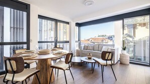 Een moderne eethoek met een ronde houten tafel, stoelen en uitzicht op gebouwen door grote ramen.