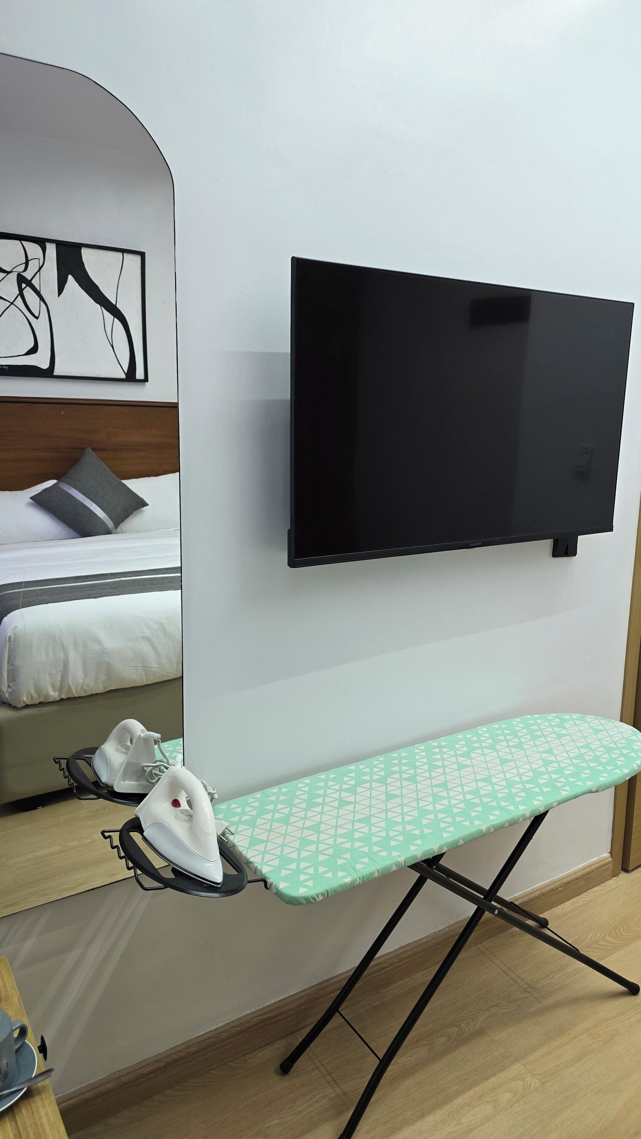 Una habitación con una cama, un televisor de pantalla plana montado en la pared y un centro de planchado con tabla y dos planchas.