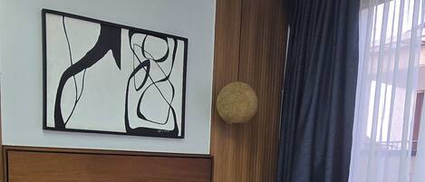A hotel room with a large bed, a headboard, a wall-mounted artwork, a round wall clock, and a window with curtains.