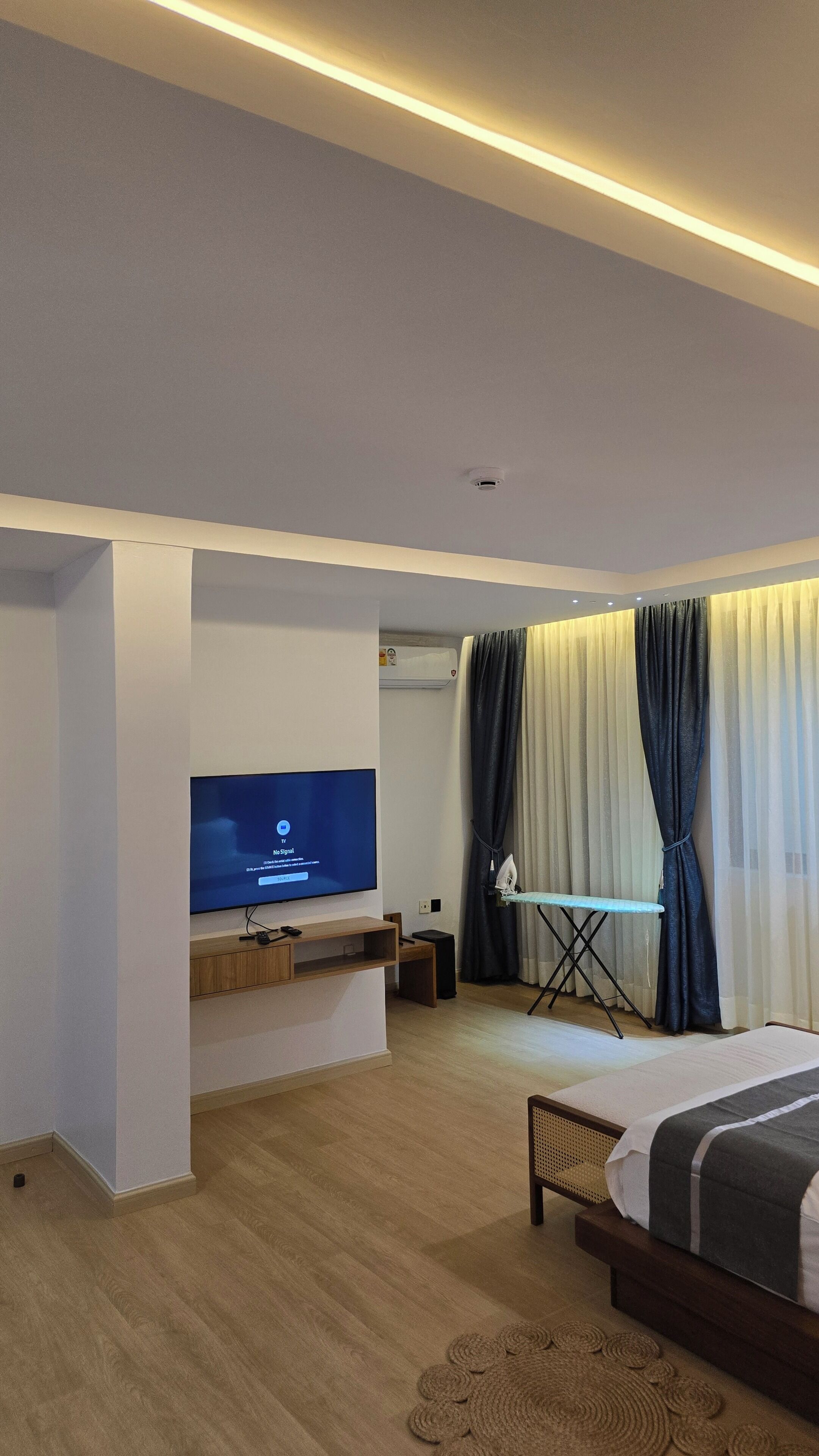 Une chambre moderne équipée d’un téléviseur à écran plat, d’un lit, d’une petite table et d’un appareil de climatisation fixé au plafond.
