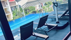 A poolside area with lounge chairs, umbrellas, and a view of a building with balconies and greenery. - Eza Hotel (Kigali)