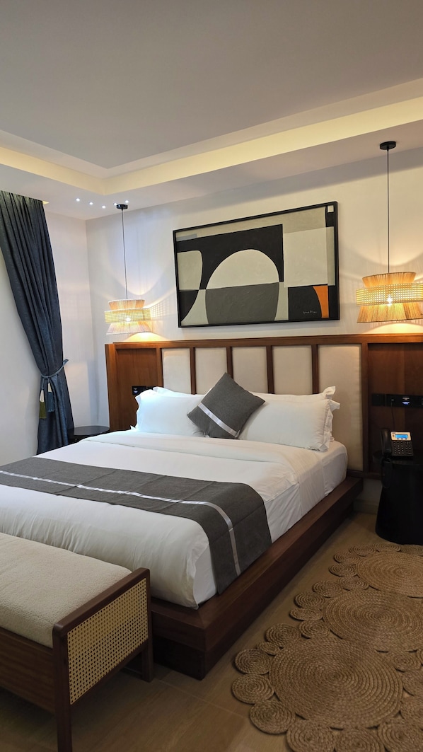 A modern hotel room with a large bed, a bedside table with a phone, a wall-mounted artwork, and a decorative lamp. - Eza Hotel (Kigali)