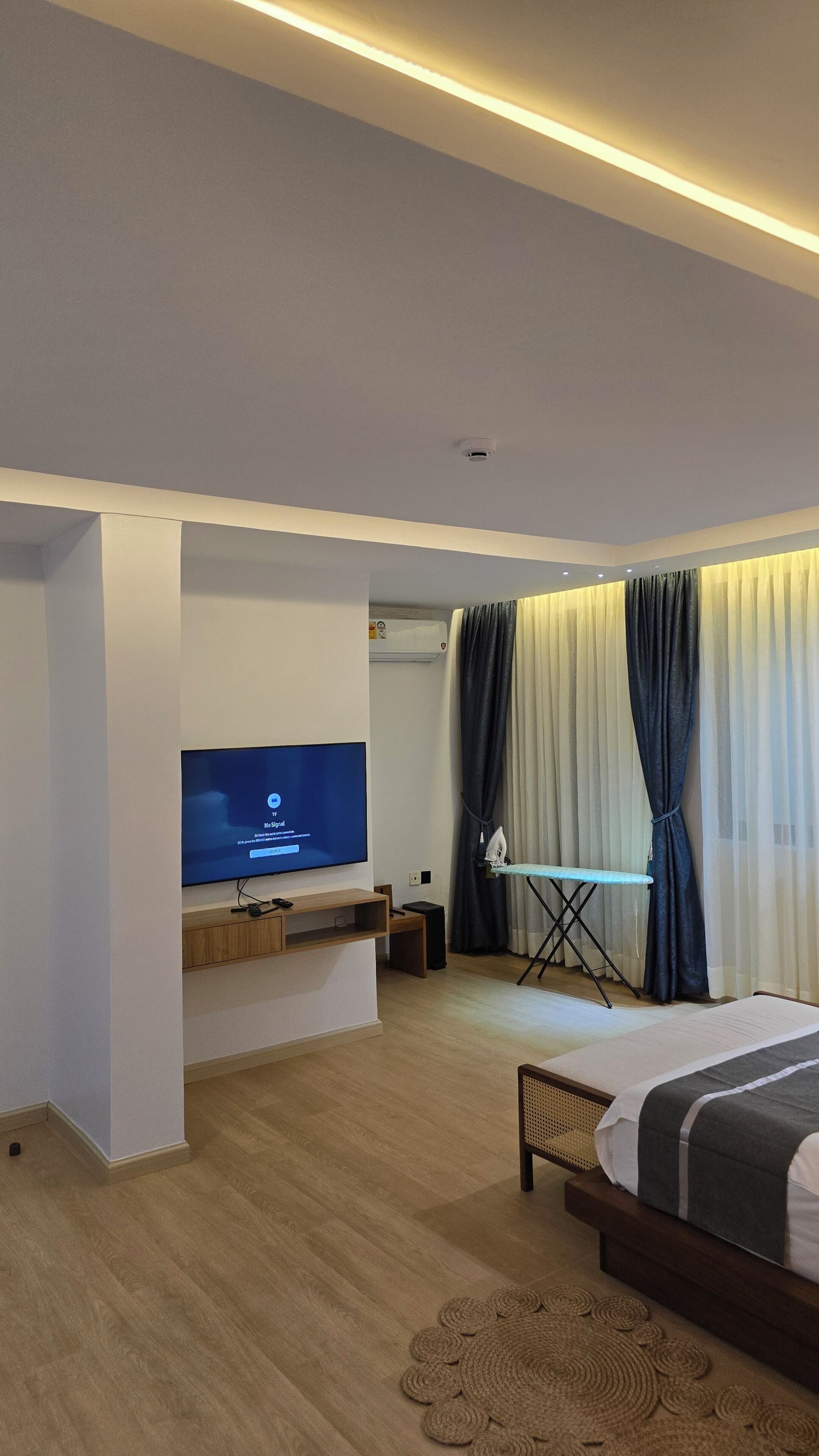 A modern hotel room with a flat-screen TV, a foldable table, a bed, and a ceiling-mounted air conditioning unit.