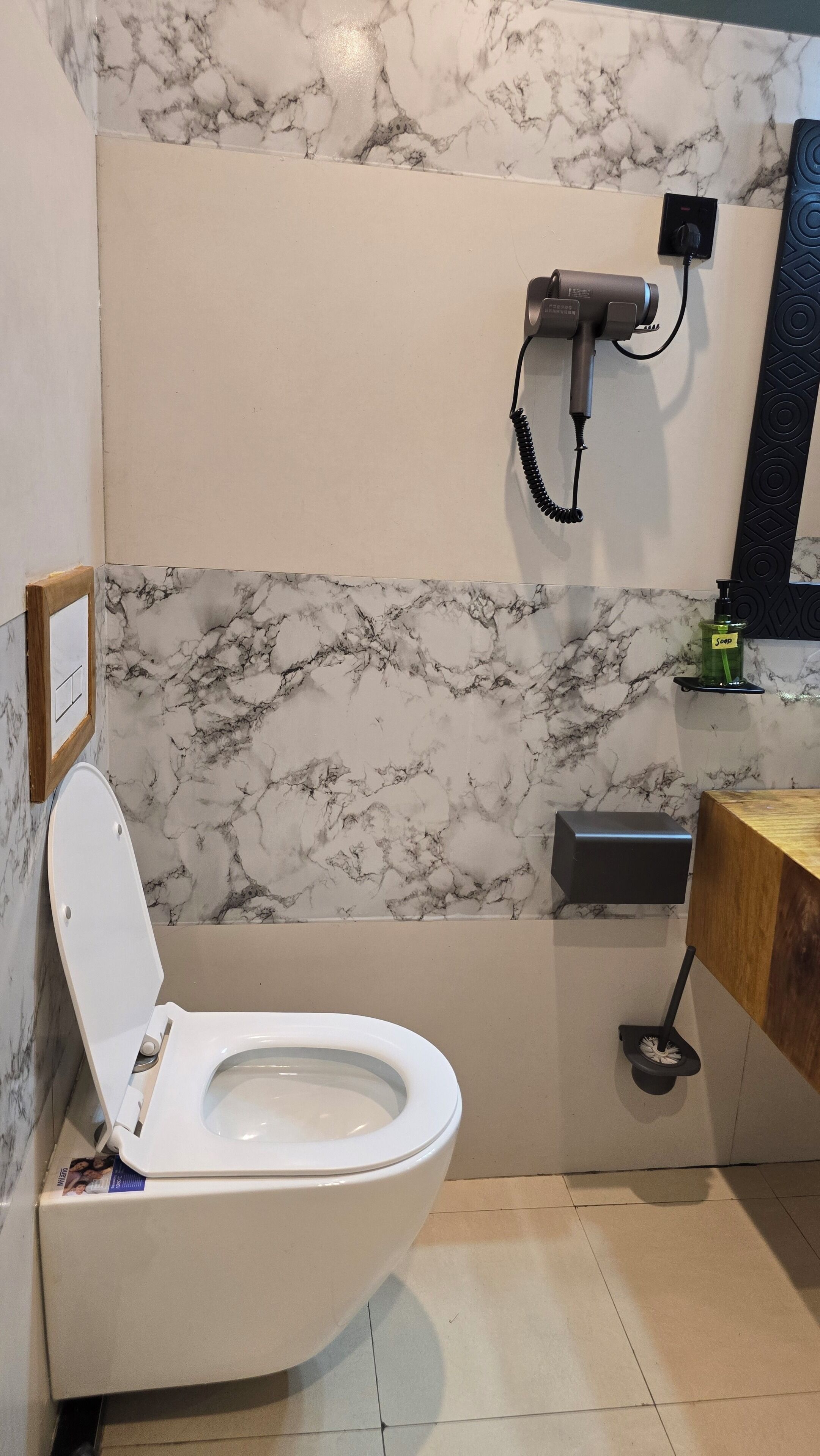 A bathroom with a white toilet, a hairdryer on a wall-mounted stand, a soap dispenser, and a toilet brush.