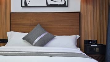 Habitación de hotel con una cama grande, un cuadro abstracto moderno, cabecera de madera, mesita de noche con lámpara y panel de control.