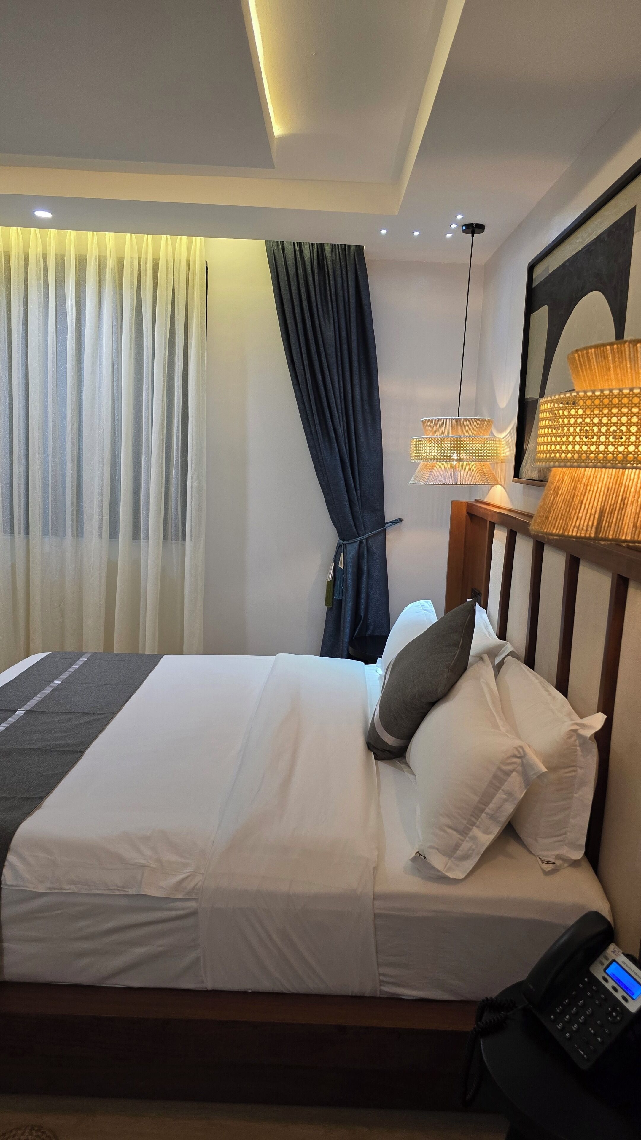 A hotel room with a bed, a bedside telephone, a lamp, and a curtain.