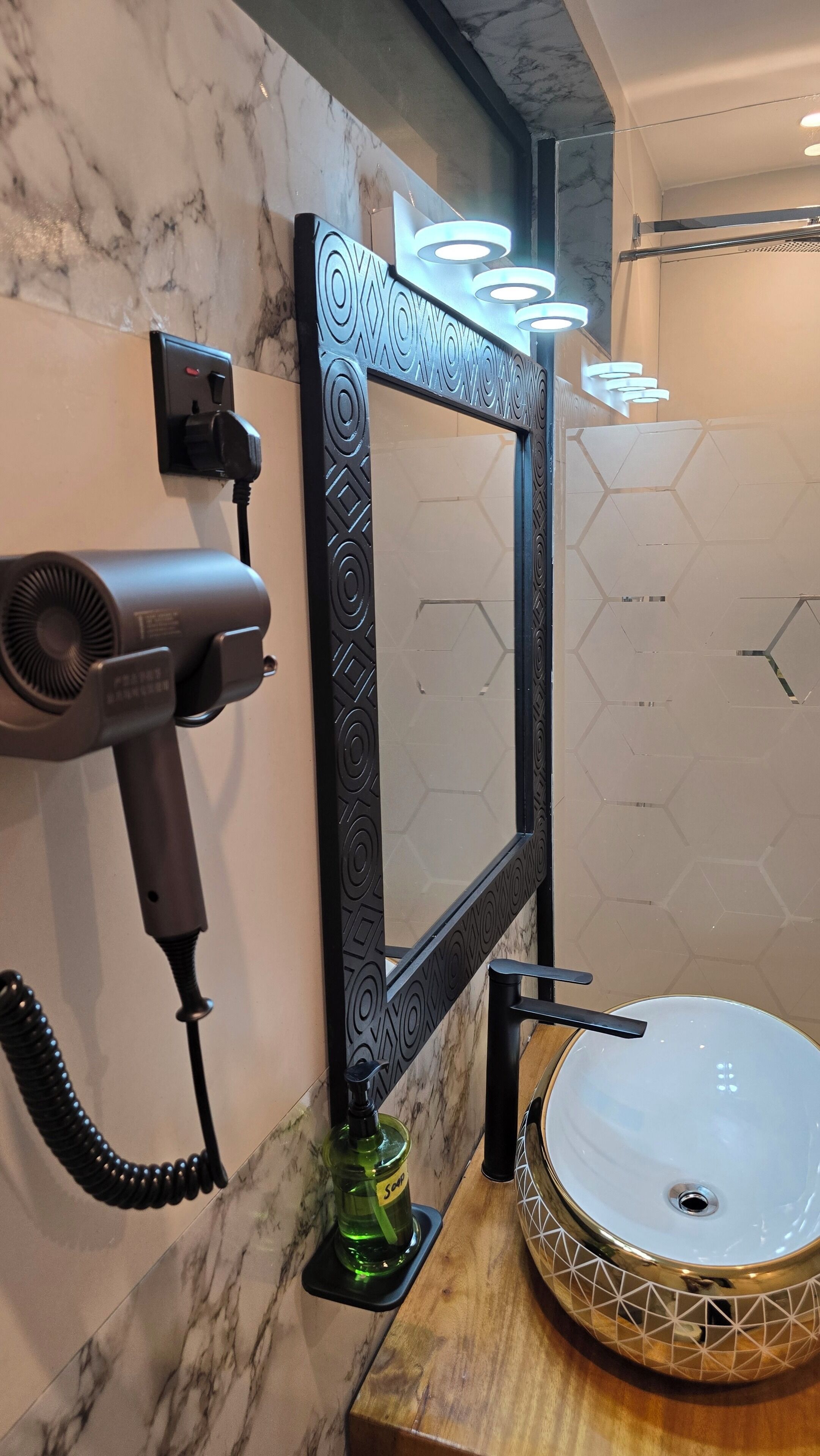 A bathroom with a marble wall, a hairdryer, a mirror with decorative frame, and a round sink with a geometric pattern.