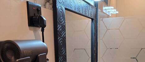 A bathroom with a marble wall, a hairdryer, a mirror with decorative frame, and a round sink with a geometric pattern.
