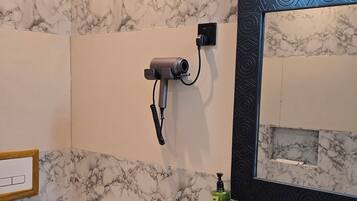Un baño con inodoro, lavabo de mármol y secador de pelo en un soporte de pared, además de un espejo con marco negro.