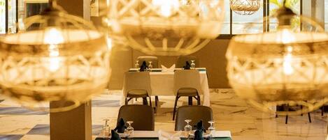 A restaurant with a marble floor, round tables, and hanging spherical chandeliers.