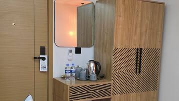 A room with a wooden wardrobe, a desk with a mirror, an ironing board, and a wall-mounted air conditioner.