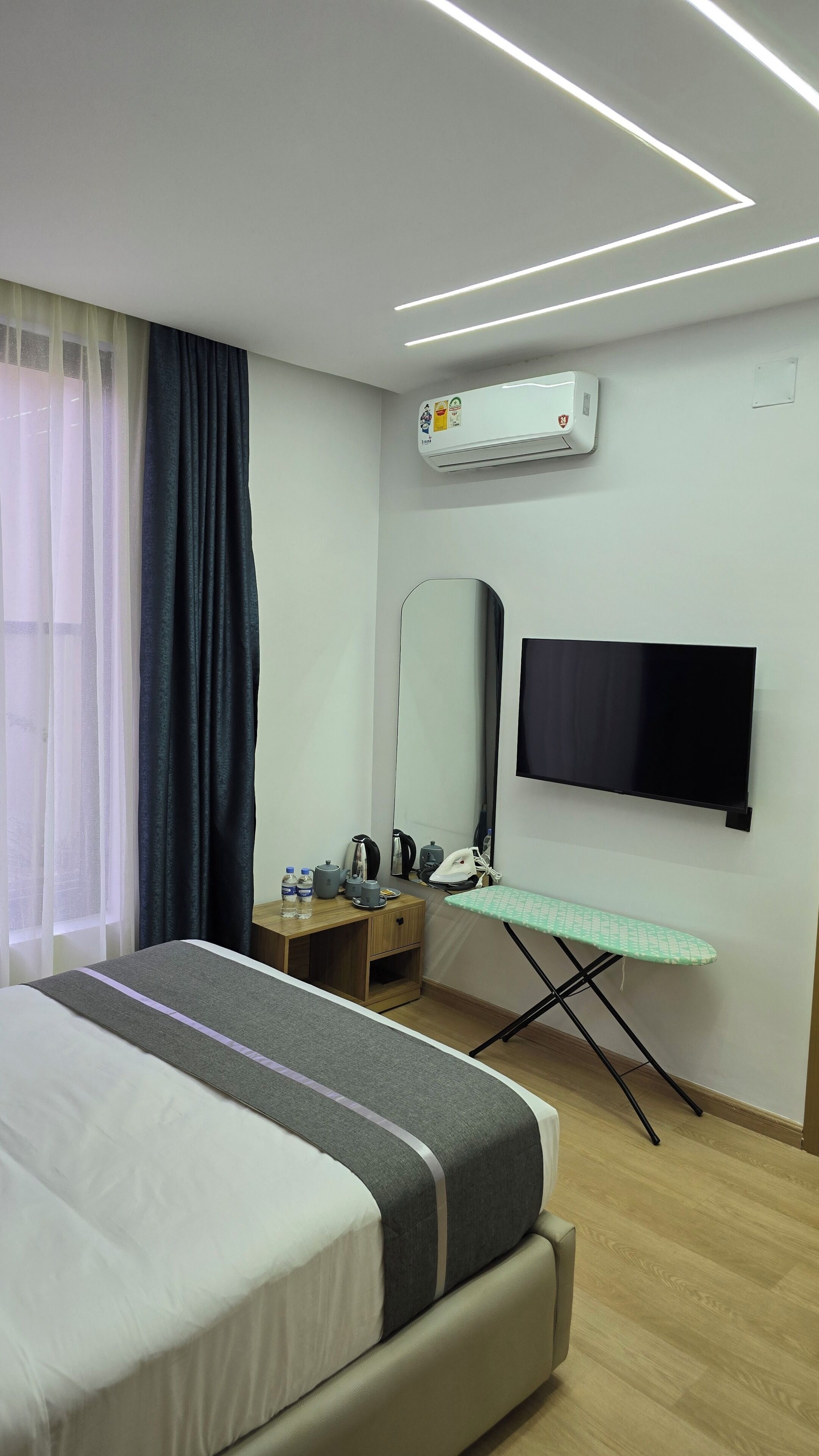 A modern hotel room with a bed, an ironing board, a flat-screen TV, and an air conditioning unit.