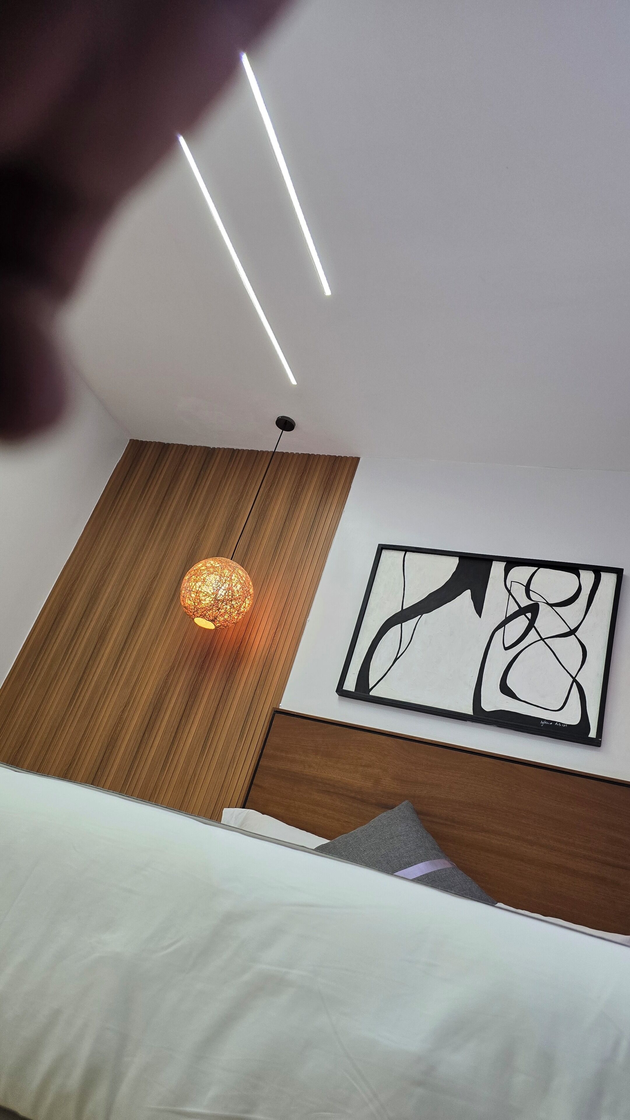 Une chambre à coucher avec un lit, un luminaire suspendu, une tête de lit en bois et un tableau abstrait accroché au mur.