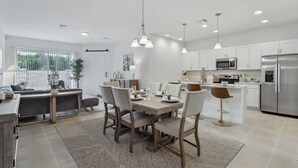 A modern kitchen with white cabinets, stainless steel appliances, and a dining area with a table set for four. - Kissimmee Oasis 4BR House Pool & Sleeps 8 (Kissimmee)