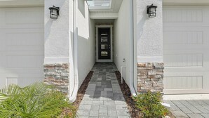A house with a covered walkway, stone accents, and two garage doors. - Kissimmee Oasis 4BR House Pool & Sleeps 8 (Kissimmee)
