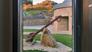 A window with a view of a stone building, a large rock, and a metal sculpture. - Casa Rustica O Facho (Cangas)