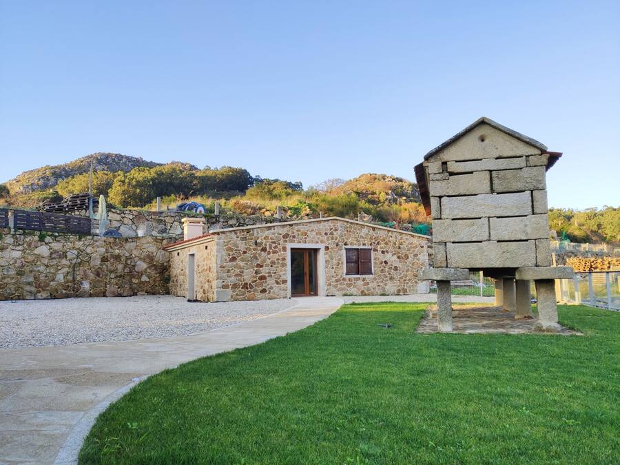 Un bâtiment en pierre doté d’une porte et d’une fenêtre, entouré d’un mur de pierre et d’une zone herbeuse.