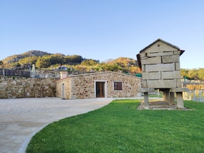 A stone building with a door and window, surrounded by a stone wall and a grassy area.