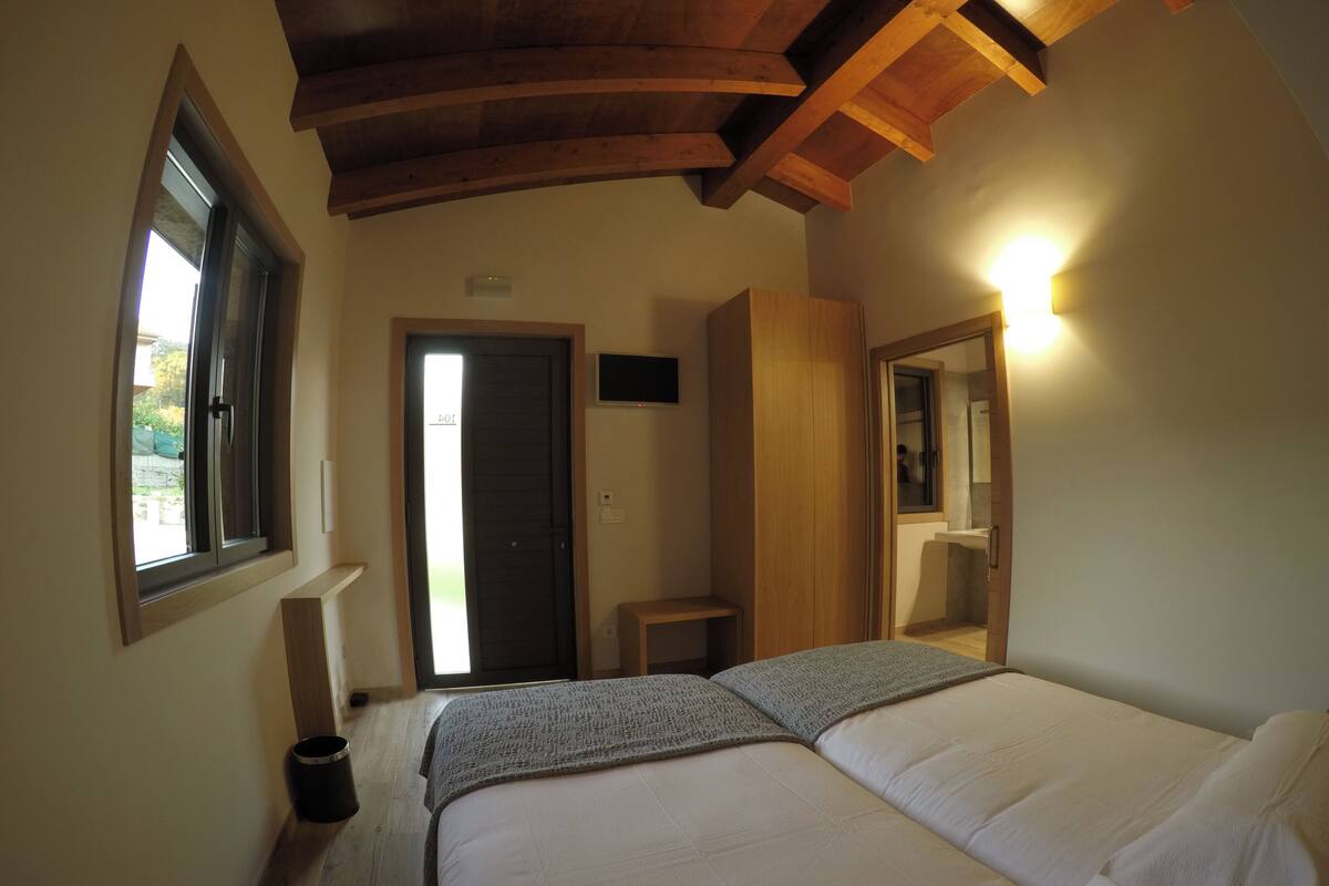 A bedroom with a bed, a window, a door, a mirror, and a small table.