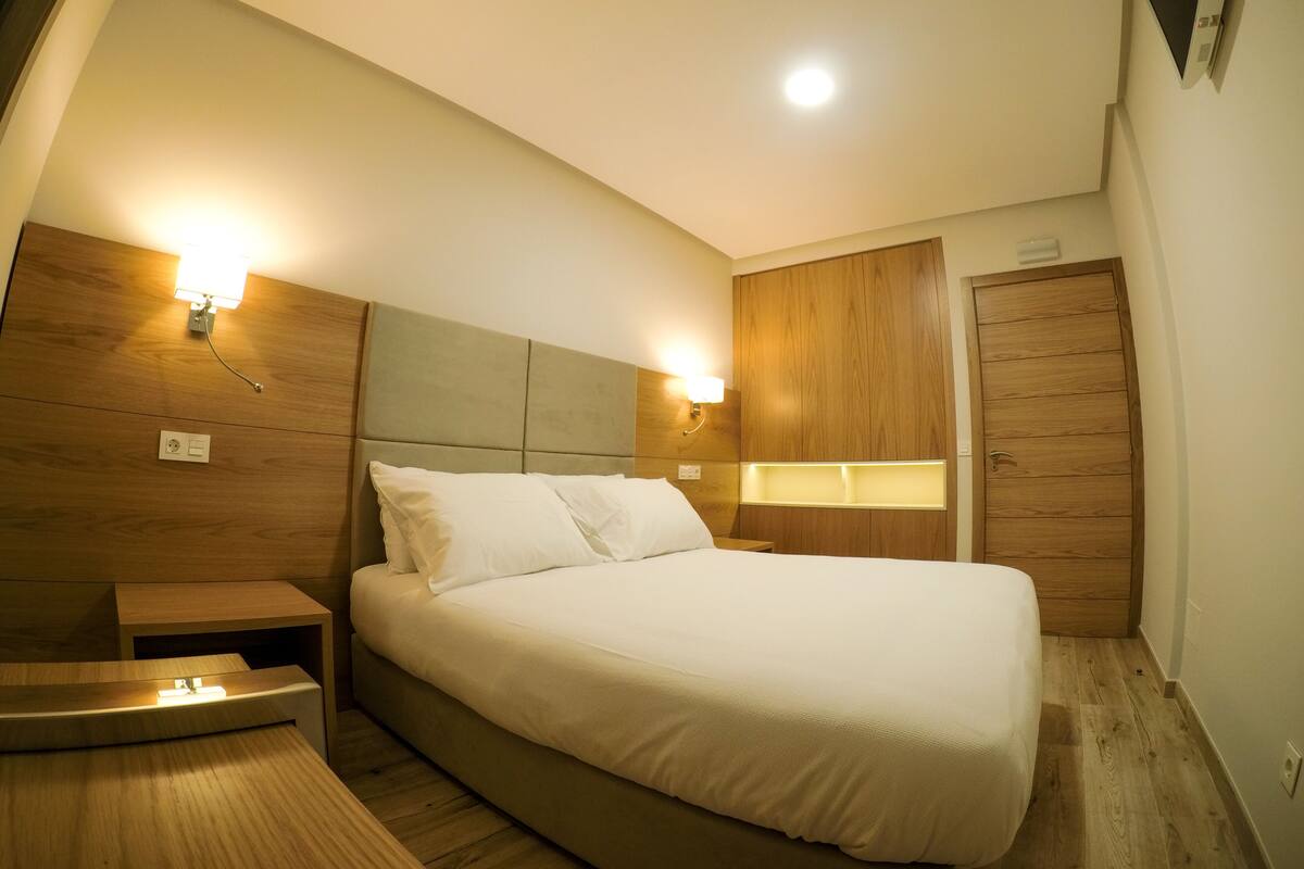 A bedroom with a bed, bedside tables, a wooden wardrobe, and wall-mounted lighting.