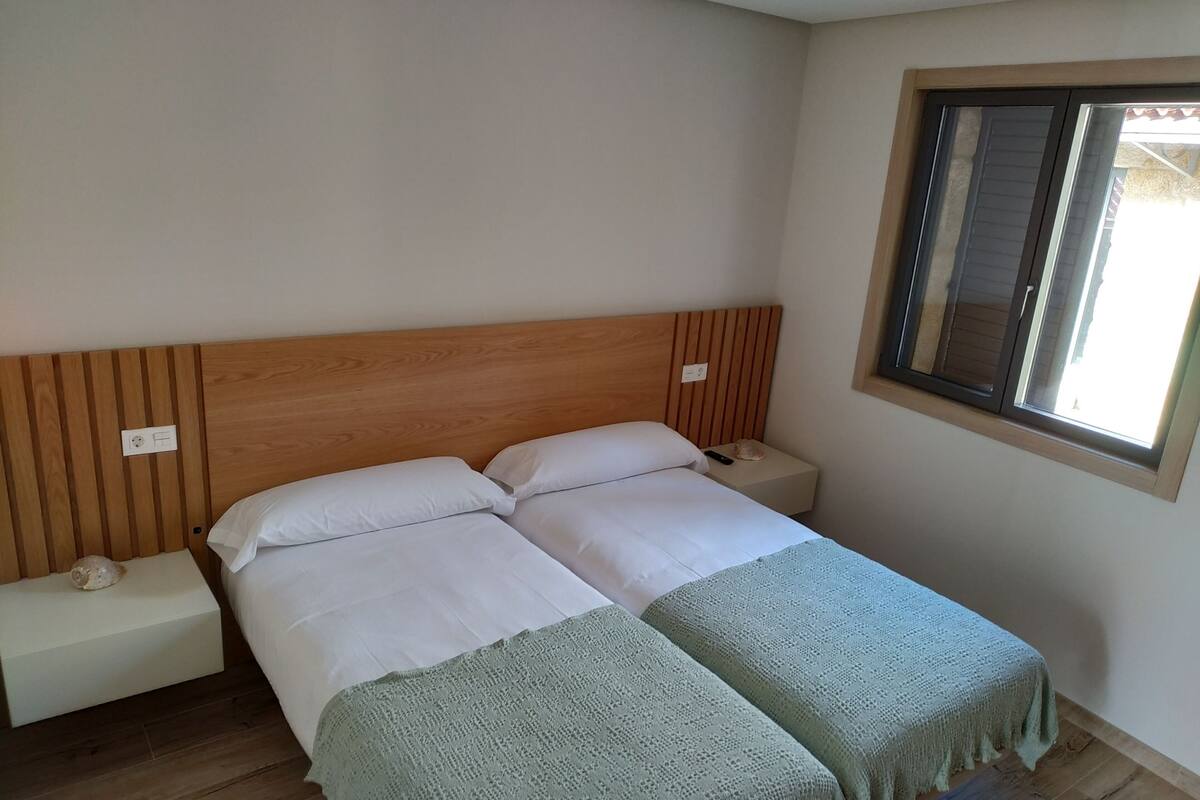 A double bed with a wooden headboard, a bedside table with a lamp, and a window with blinds.