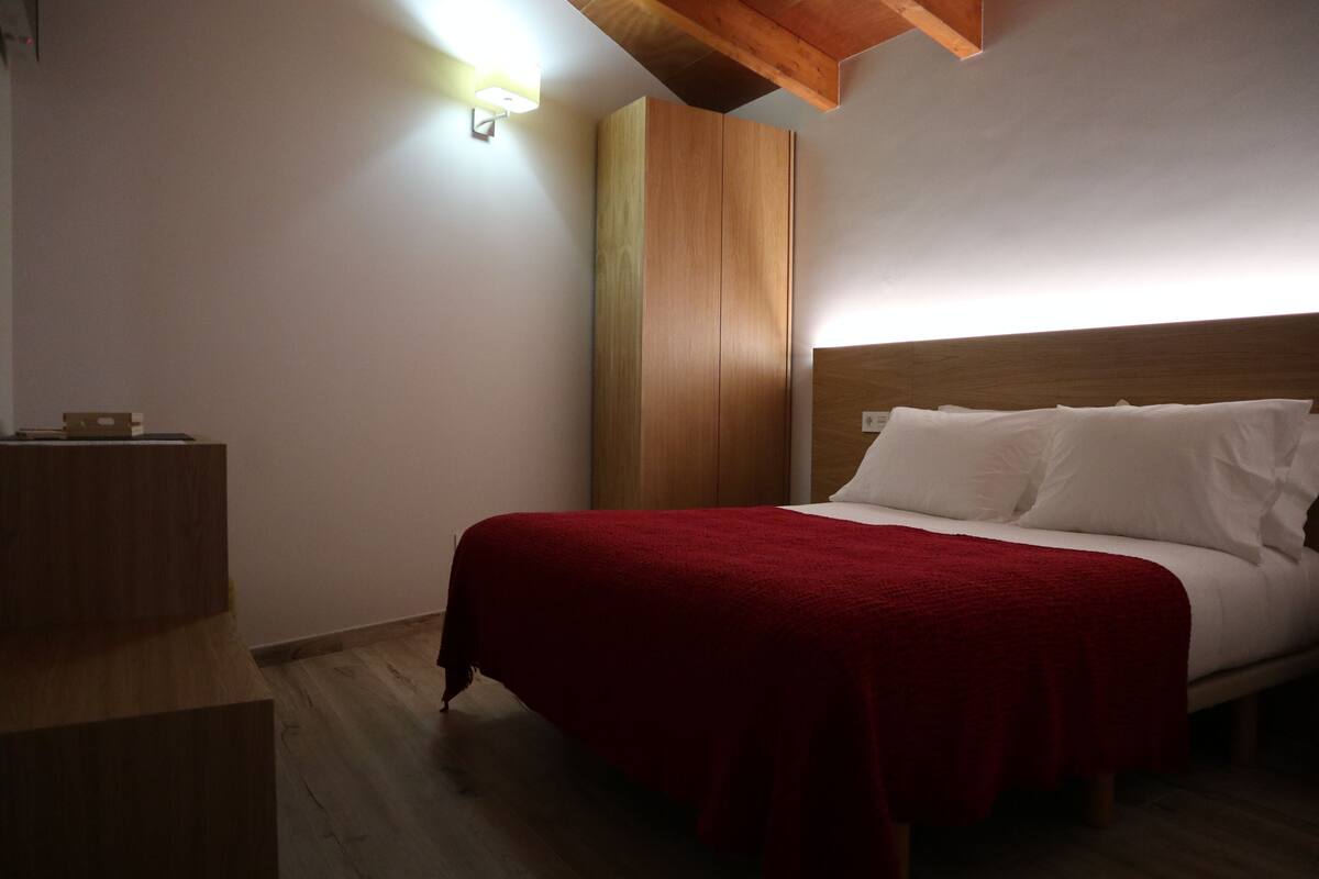 A bedroom with a wooden headboard, a red bedspread, and a nightstand.