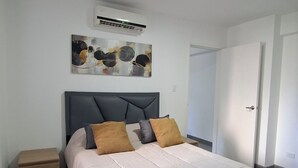 Une chambre à coucher avec un lit, une table de chevet, un tableau et un appareil de climatisation.