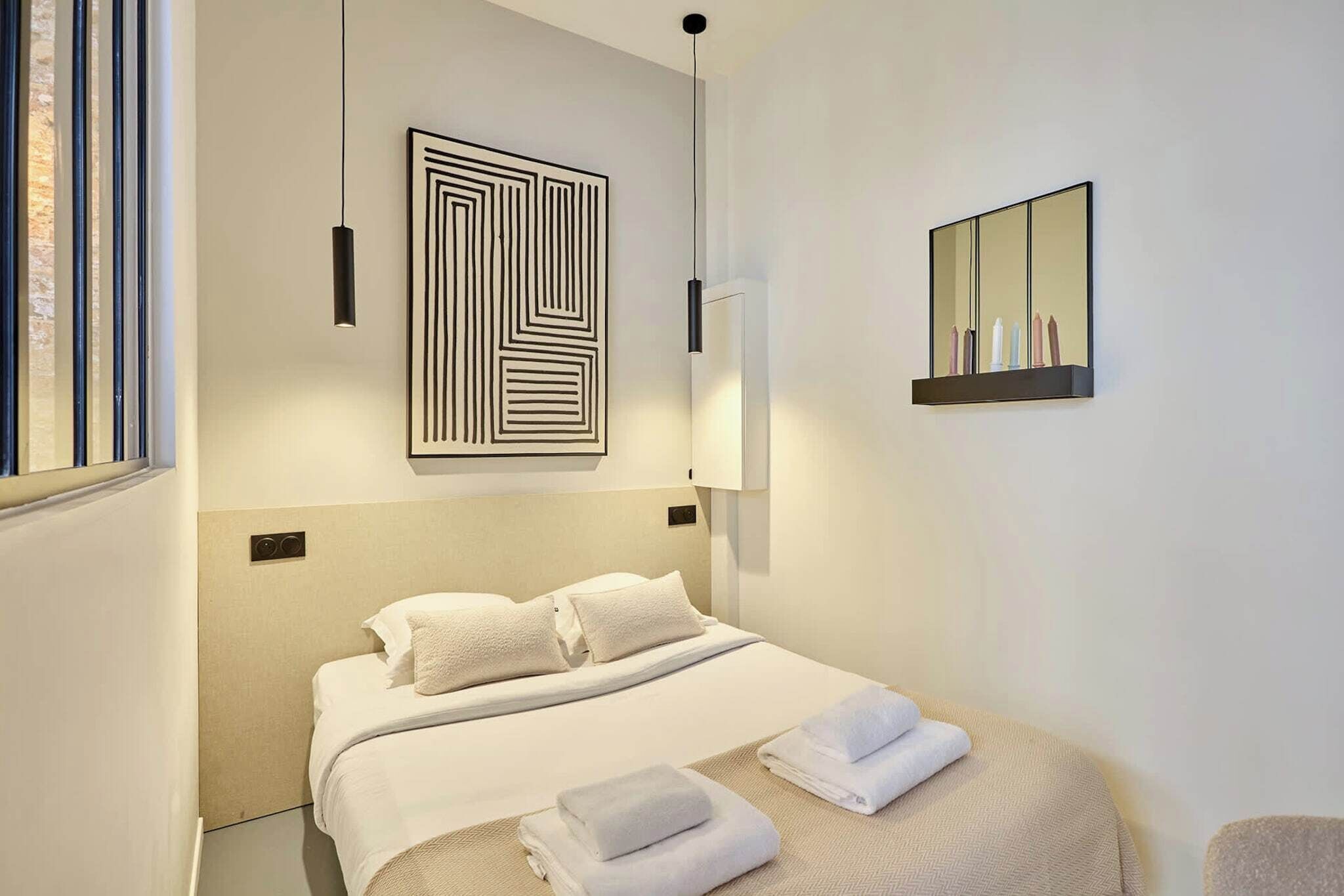 Ett modernt hotellrum med en stor säng, ett geometriskt konstverk på väggen, en spegel och ett nattduksbord.