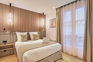 Ein Hotelzimmer mit einem großen Bett, Nachttischen, einem Holz-Kopfteil, einem gerahmten Bild und transparenten Vorhängen.