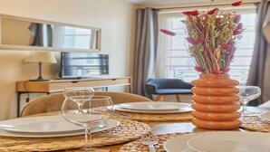 A dining area with a table set for two, a vase with flowers, and a television in the background. - Lovely apartement  with AC - Center of Paris (Paris)