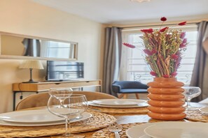 A dining area with a table set for two, a vase with flowers, and a television in the background. - Lovely apartement  with AC - Center of Paris (Paris)