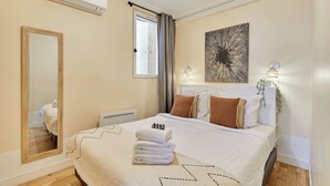 A hotel room with a bed, a large mirror, a window with curtains, a wall-mounted air conditioner, and a decorative wall piece. - Lovely apartement  with AC - Center of Paris (Paris)