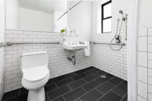 A modern bathroom with white subway tiles, a white toilet, a sink with a mirror, and a shower area. - Relaxing 2 Beds|Midtown Times Square (New York)