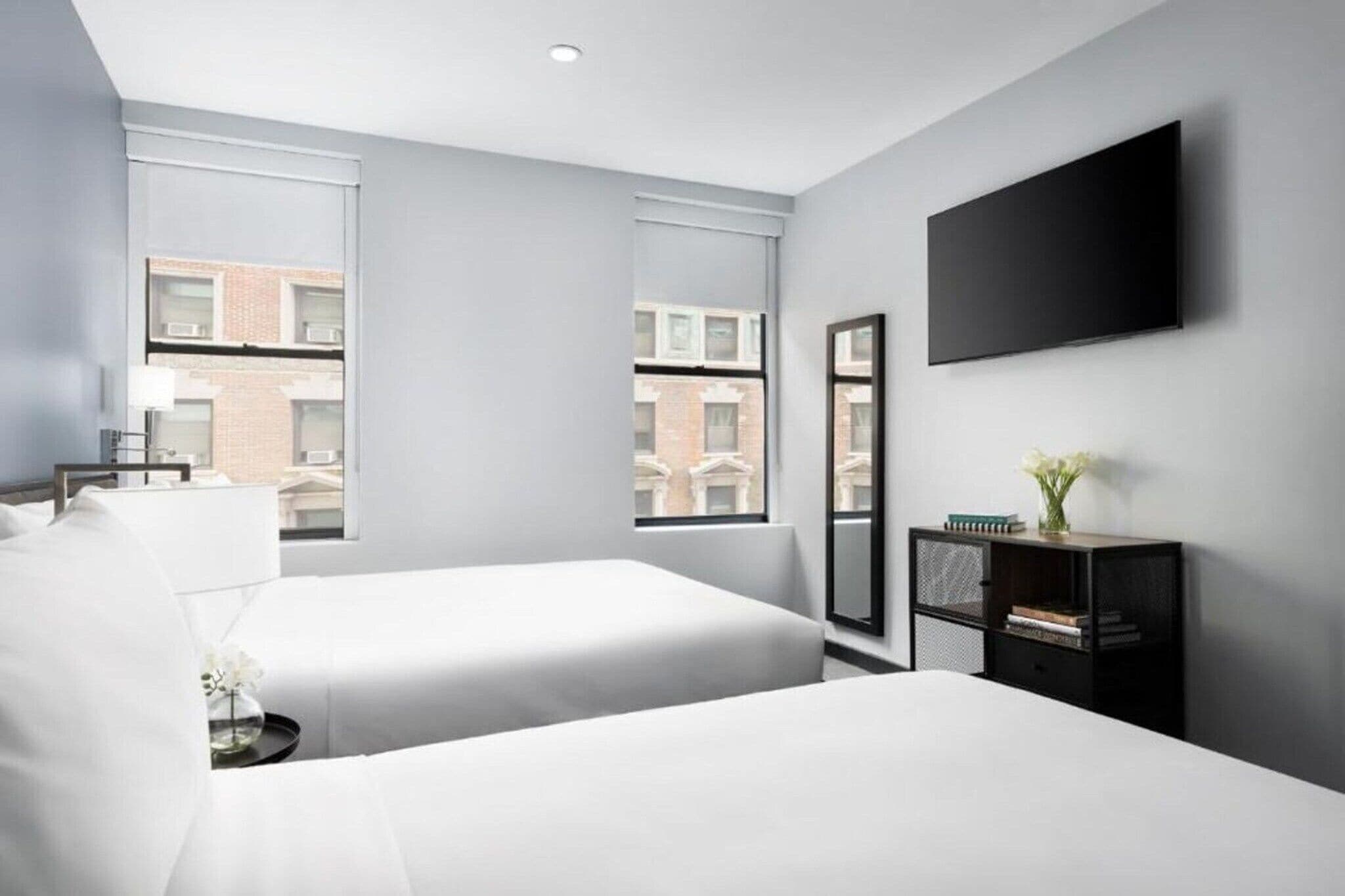 Een moderne hotelkamer met twee bedden, een flatscreen televisie, een klein bijzettafeltje en een boekenplank.